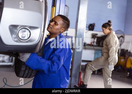 afroamerikanische mittlere Erwachsene weibliche Mechanikerin, die Auto repariert, mit einer asiatischen Kollegin, die im Hintergrund arbeitet Stockfoto