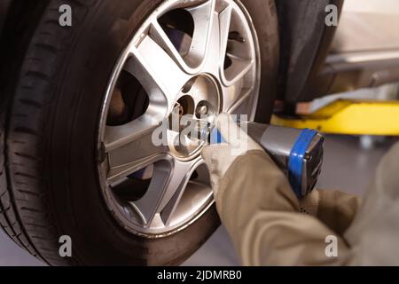 Zugeschnittenes Bild einer weiblichen asiatischen Mechanikerin mit mittlerem Erwachsenen, die ein Arbeitswerkzeug verwendet, während sie den Autoreifen repariert Stockfoto