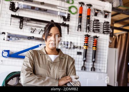 Porträt einer selbstbewussten asiatischen mittleren erwachsenen Mechanikerin gegen verschiedene Arbeitswerkzeuge in der Werkstatt Stockfoto