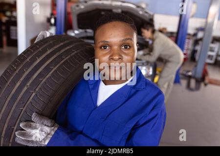 Porträt einer selbstbewussten, mittleren erwachsenen afroamerikanischen Mechanikerin, die Autoreifen in der Werkstatt trägt Stockfoto