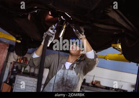 Mittlere Erwachsene asiatische Schweißerinnen Schweißen während der Reparatur Auto unter Autoaufzug in der Werkstatt Stockfoto