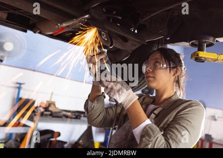 Mittlere Erwachsene asiatische weibliche Schweißer mit Arbeitswerkzeug während der Reparatur Auto in der Werkstatt Stockfoto