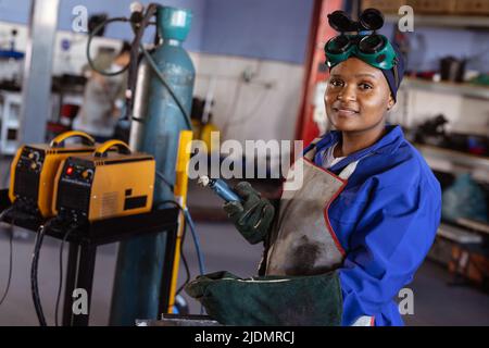 Porträt einer selbstbewussten lächelnden afroamerikanischen Schweißerin mit mittlerem Erwachsenen, die in der Werkstatt arbeitet Stockfoto