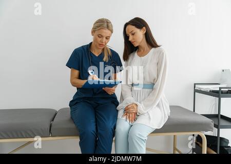 Der Arzt füllt das Formular für den medizinischen Bericht über die medizinische Versorgung von Patienten während der Verabredung aus Stockfoto