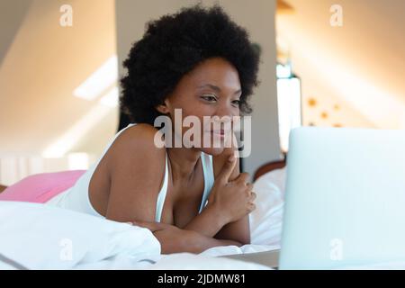 Afro junge afroamerikanische Frau, die im Schlafzimmer Videos auf dem Laptop ansieht, Platz kopieren Stockfoto