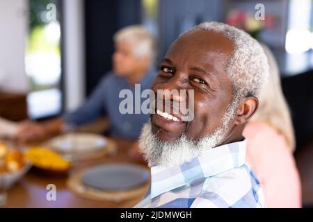 Nahaufnahme des afroamerikanischen Senioren-Mannes mit multirassischen Freunden, die am Esstisch sitzen Stockfoto