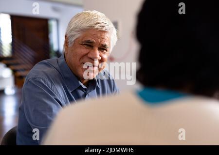 Lächelnder älterer Mann aus der Birazialzeit, der sich mit einer Freundin unterhielt, während er im Pflegeheim zum Mittagessen saß Stockfoto