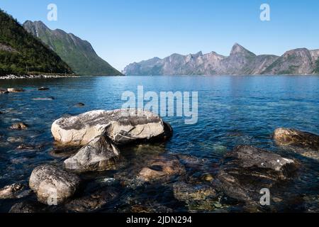 Felsiger Strand von Senja, Norwegen, mit Berggipfeln im Hintergrund an einem sonnigen Sommertag Stockfoto