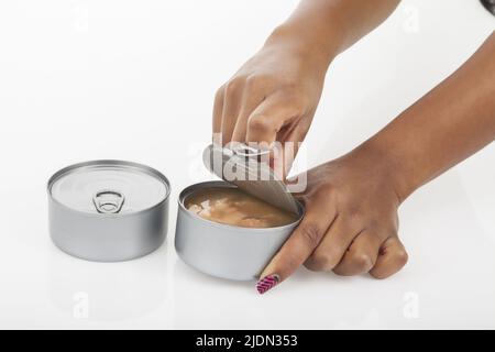 Weibliche Hände öffnen Dose von Thunfisch; Foto auf weißem Hintergrund. Stockfoto