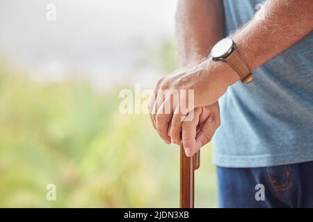 Ein älterer behinderter Mann hält einen Stock im Park eines Pflegeheims. Nahaufnahme eines älteren Mannes, der eine Gehhilfe im Freien hält und sich an einem entspannt Stockfoto