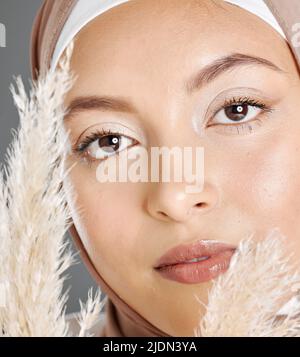 Nahaufnahme Porträt Gesicht der schönen jungen muslimischen Frau trägt natürliches Make-up und Kopftuch posiert mit Pampas Weizenpflanze vor Studio-Hintergrund Stockfoto