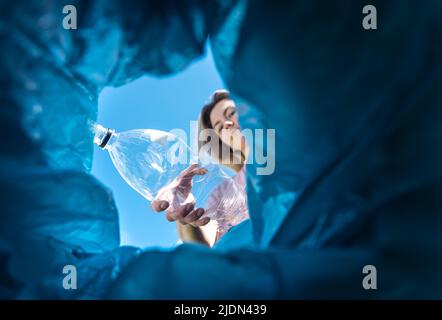 Eine Frau wirft eine Plastikflasche in den Müll. Nahaufnahme aus dem Mülleimer Stockfoto