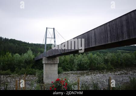 Holzbrücke über den Fluss Taro in Borgo Val di Taro, Provinz Parma, Italien. Brücke auf Betonsäule über Bergfluss mit niedrigem Wasser Stockfoto