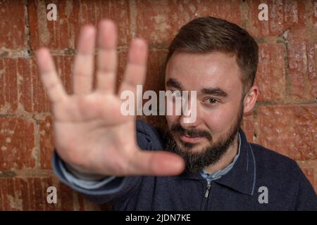Junger bärtiger Mann lächelt fröhlich und fröhlich, winkt mit der Hand, begrüßt und begrüßt Sie oder sagt Auf Wiedersehen. Hochwertige Fotos Stockfoto