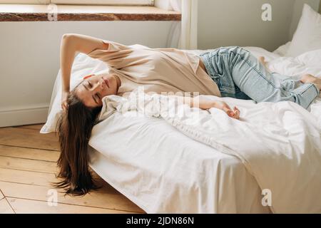 Traurig gelangweilt entspannte junge Frau mit langen Haaren liegt auf dem Bett, Konzept von Depression und Schwermut Stockfoto