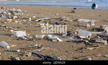 Plastikverschmutzung am Meeresstrand. Abfall bei Flut mit Meereswellen im Hintergrund. Umwelt- und Meeresplastik-Verschmutzung. Verschiedene Arten Stockfoto
