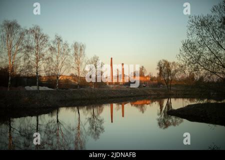 Blick auf die Fabrik. Ziegelrohre der Anlage. Landschaft mit See und Birken. Industrieanlage. Stockfoto