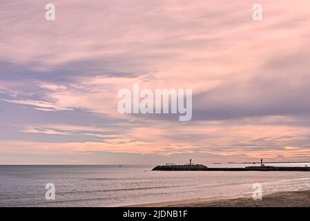 Ein Wellenbrecher am Strand im Mittelmeer mit kleinen boats.bright Tagen, weißen Wolken, orangefarbenen Tönen, ruhigem Meer, keine Menschen Stockfoto