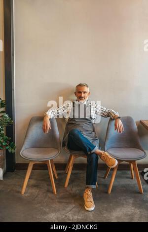 Mann, der auf einem Stuhl sitzt und auf die Kamera schaut Stockfoto