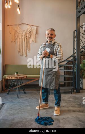 Mann, der den Mopp hält, lächelt in der Kamera im Café Stockfoto