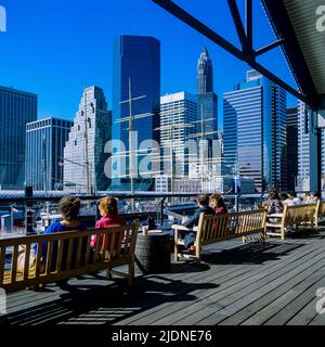 New York 1980s, Menschen entspannen sich auf Bänken am Pier 17, South Street Seaport, Wolkenkratzern, Skyline von Lower Manhattan, New York City, NYC, NY, USA, Stockfoto