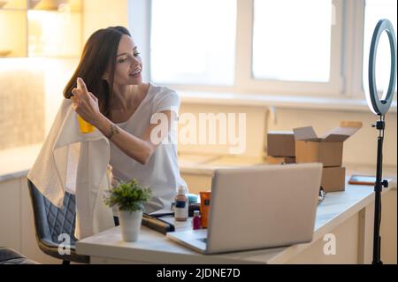 Frau spritzt Haarspray posiert vor dem Laptop Stockfoto