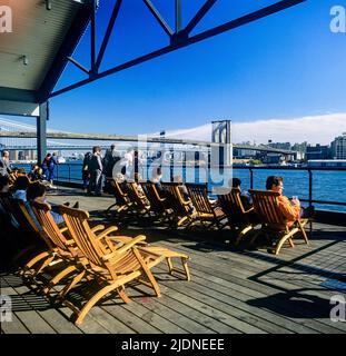 New York 1980s, Menschen entspannen sich auf Liegestühlen von Pier 17, South Street Seaport, Brooklyn Bridge, Lower Manhattan, New York City, NYC, NY, USA, Stockfoto