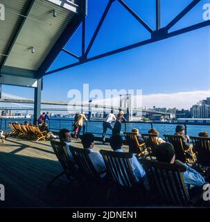 New York 1980s, Menschen entspannen sich auf Liegestühlen von Pier 17, South Street Seaport, Brooklyn Bridge, Lower Manhattan, New York City, NYC, NY, USA, Stockfoto