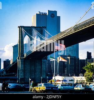 New York 1980er Jahre, Brooklyn Bridge, River Cafe Terrasse, Flags, New York, Telefongesellschaft Gebäude mit Bell Atlantic Logo, in der Ferne, Golden Hour, Manhattan, New York City, NY, NYC, USA, Stockfoto