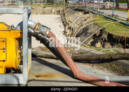 Große, tragbare, gelbe elektrische Wasserpumpe mit Schlauch zur Entwässerung der tiefen Grube des Gebäudefundaments Stockfoto