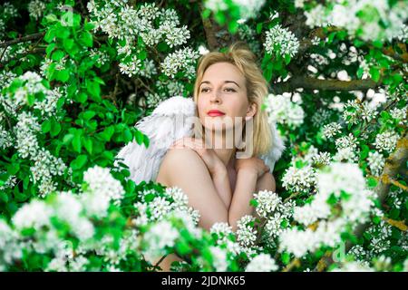 Schöne weibliche Frau mit weißen Flügeln mit weißen Frühlingsblumen. Stockfoto