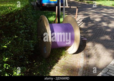 Holztrommel mit dünnem violettem Glasfaserkabel am Straßenrand des niederländischen Dorfes Bergen. Juni, Stockfoto