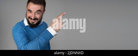 Hübscher gesunder junger Mann, der lächelt, wobei sein Finger isoliert auf weißem Banner-Hintergrund mit Kopierraum zeigt. Hochwertige Fotos Stockfoto