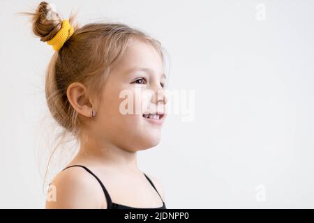 Niedliches, kleines, blondes Mädchen mit Zöpfen, das lächelnd jemanden ansieht Stockfoto