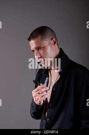Ein junger, attraktiver Mann, der ein schwarzes Hemd und eine Sonnenbrille trägt Stockfoto