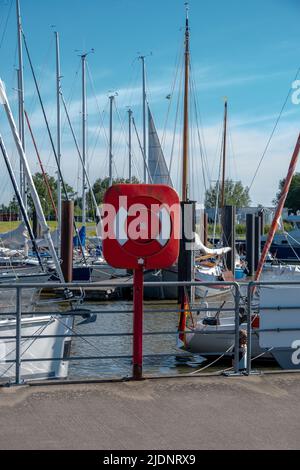 Glückstadt, Schleswig-Holstein Deutschland - 06 03 2022: Ein Rettungsring im Hafen von Glückstadt mit Segelbooten und Masten im Hintergrund Stockfoto