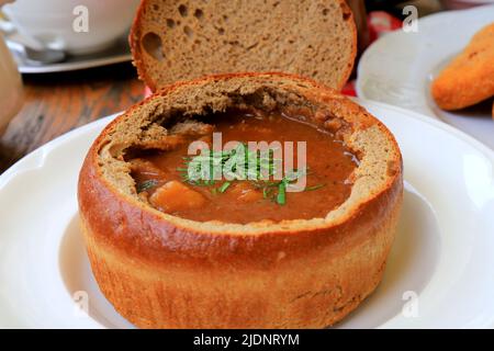 Originalgericht - Gulaschsuppe im Brottopf, Teller im Restaurant, Café. Köstliche herzhafte Fleischgericht der tschechischen, bulgarischen, rumänischen Küche, europäische Stockfoto