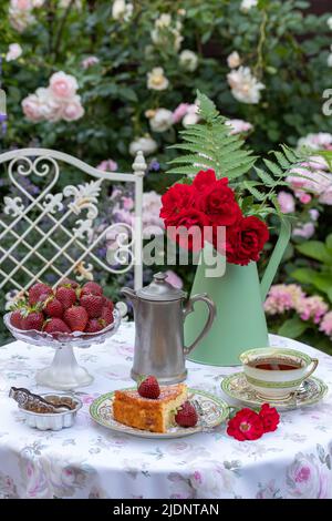 In der Lage Dekoration mit Stück Kuchen, Erdbeeren, Vintage-Porzellan und Strauß Rosen im Sommergarten Stockfoto