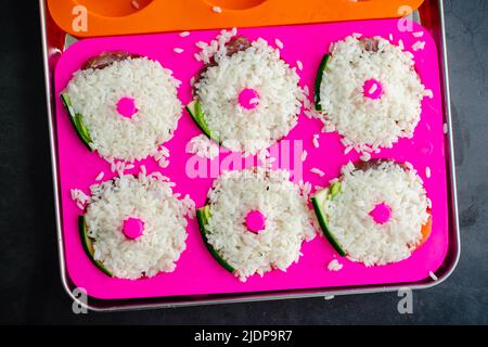 Donut-förmiges Sushi in einer Silikonform zubereiten: Sushi-Reis, der über frischem Fisch und Gemüse zu einer Donut-Form gepresst wird Stockfoto