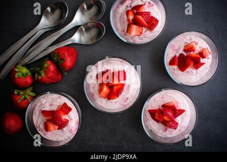 Gerichte mit Erdbeer-Käsekuchen-Mousse: Individuelle Fruchtdesserts in Glasschüsseln mit Löffeln Stockfoto