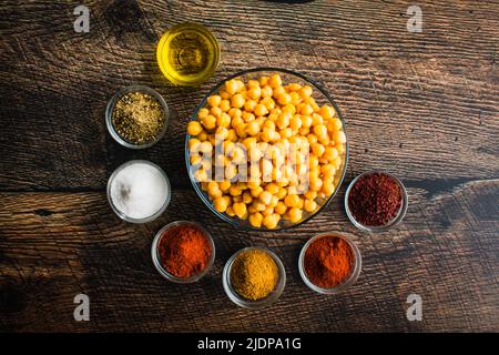 Zutaten für Sumac und Gewürz geröstete Kichererbsen: Ansicht von Garbanzo-Bohnen aus der Dose, Olivenöl und Gewürzen in kleinen Glasschüsseln Stockfoto