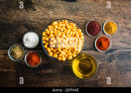 Zutaten für Sumac und Gewürz geröstete Kichererbsen: Ansicht von Garbanzo-Bohnen aus der Dose, Olivenöl und Gewürzen in kleinen Glasschüsseln Stockfoto