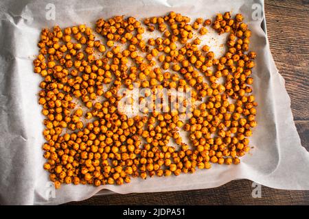 Gewürzte Kichererbsen auf einem mit Pergament ausgekleideten Blech Pfanne: Garbanzo-Bohnen vor dem Rösten in Sumac und anderen Gewürzen geschwenkt Stockfoto