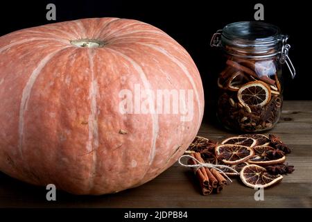 Frischer Bio-Kürbis und weihnachtliche Gewürze in einem Glas auf dunklem Hintergrund auf einem Holztisch. Stockfoto