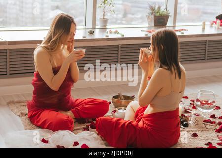 Zwei Frauen sitzen auf dem Boden und trinken Tee aus Kräutern und Blumen. Teezeremonie während der Entspannung, Entspannung, psychische Gesundheit, Harmonie Stockfoto