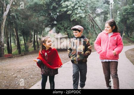 Drei Kinder, zwei Mädchen und ein Junge, die in einer Parkstraße spazieren und sich unterhalten. Stockfoto