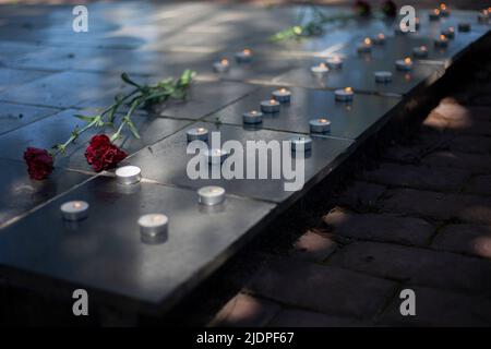 Kerzen auf Grabstein. Wachskerzen brennen auf dem Kriegsdenkmal. Zwei Blumen auf Grabstein. Begräbnisstätte der Soldaten. Memorial Complex im Detail. Stockfoto