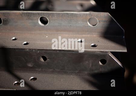 Löcher in Stahl vom Bohren. Metallrohling. Stahlprofil wird mit Bohrer in der Werkstatt gebohrt. Eisenprodukt. Löcher für die Befestigungsstruktur. Stockfoto