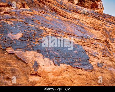 Nahaufnahme von Petroglyphen, die durch Wüstenlack geschnitzt wurden, so dass das rote Gestein des aztekischen Sandsteins durch das Petroglyph Canyon Valley of Fire Nevada leuchtet Stockfoto