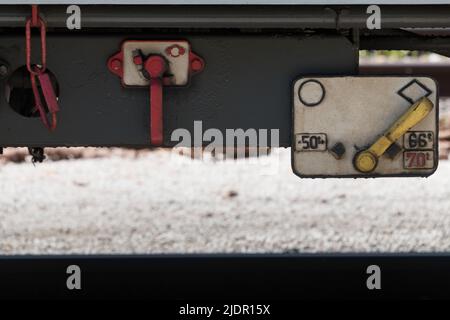 Nahaufnahme der Unterseite eines Waggons mit rot-gelben verstellbaren Hebelgriffen zum Lösen der Bremsen und zum Trennen der Stromversorgung Stockfoto